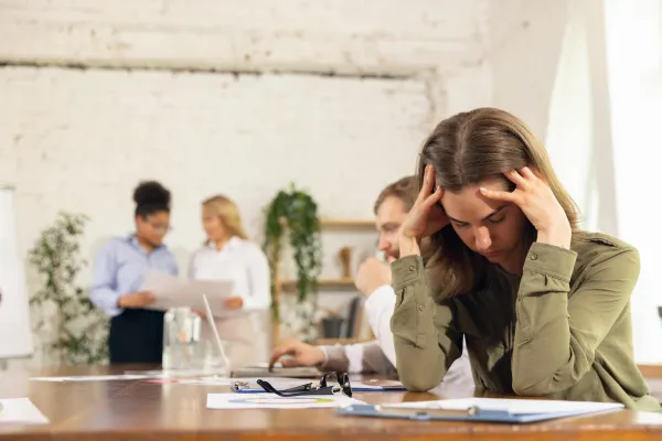 Femme visiblement fatigué qui se tiens la tête. Elle se situe d&#039;un un bureau.
